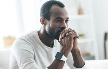 Something on his mind. Handsome young African man holding hands together and thinking while sitting on the sofa at home